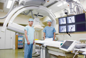 血管内治療に対応する血管撮影装置「Allura Xper FD20/20」松丸祐司部長（右）と濱田祐介技師（左）