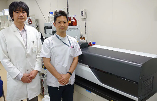 加藤隆弘准教授（左），九州大学病院検査部の瀬戸山大樹助教および研究で使用する高速液体クロマトグラフ質量分析計