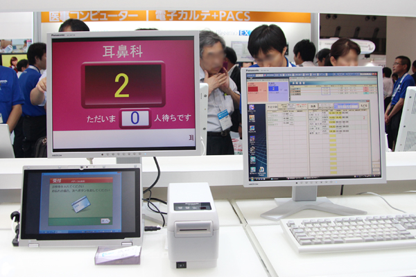 「受けNavi」と電子カルテの連携（右：受付の電子カルテ，左上：順番表示モニタ，左下：受付用のタッチパネル）