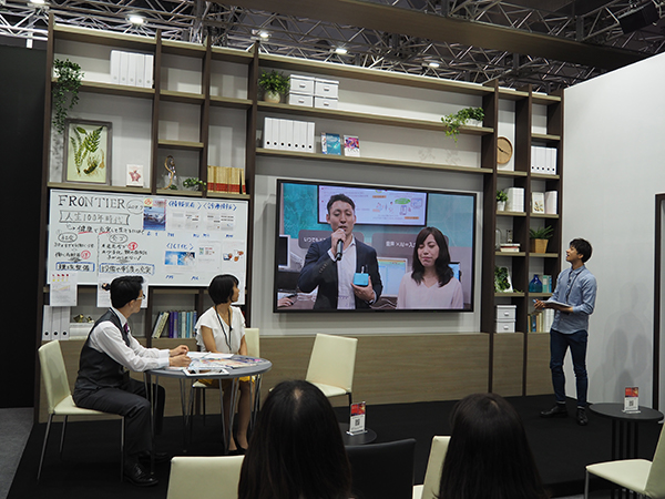 ブース内の展示コーナーからの中継がメインステージで流れる。 ブース内の展示コーナーからの中継がメインステージで流れる。