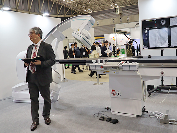 血管撮影システム「Trinias series with SCORE Opera」と音声認識機能の「SMART Voice」のデモンストレーションの様子（展示ではマイクを寝台に設置）